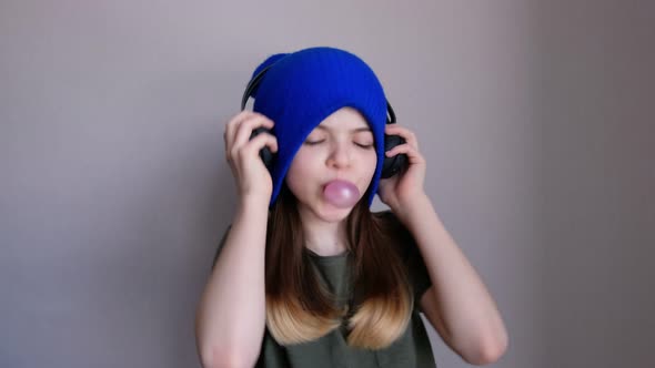 Young Girl a Teenager in a Hat Blows a Bubble of Chewing Gum and Dances