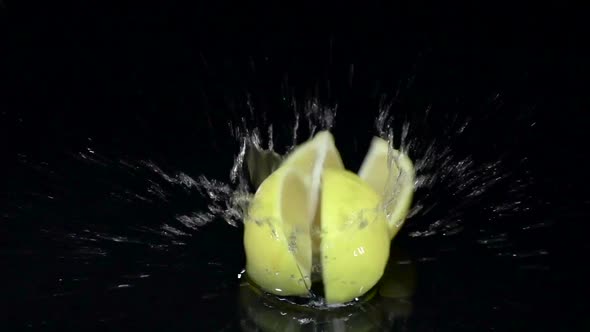 Lemon Falls Into the Water and Breaks Up Into Four Parts. Black Background. Slow Motion