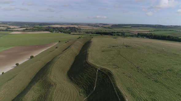 Aerial tracking down between the outer ramparts of the iron age hill fort of Maiden Castle. Sheep gr