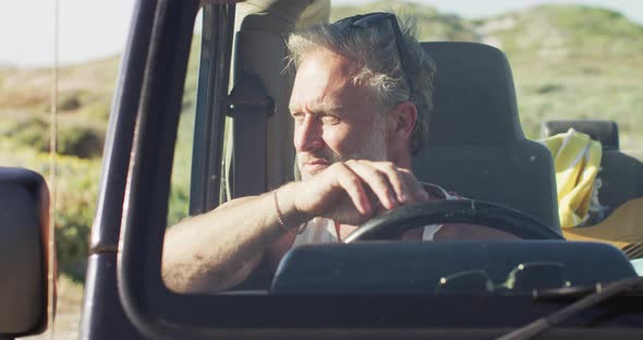 Thoughtful caucasian man sitting in car looking away on sunny day at the beach