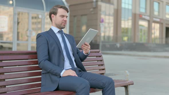 Online Video Chat on Tablet by Businessman Sitting Outdoor on Bench