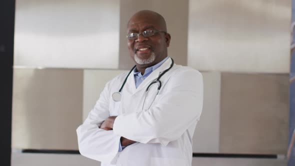 Smiling african american senior male doctor wearing white crossing his arms looking at the camera