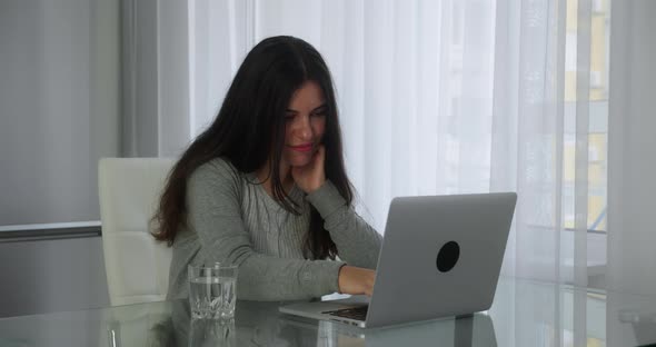 Young Woman Browsing News in Social Networks on a Laptop Sitting Workplace at Home Office