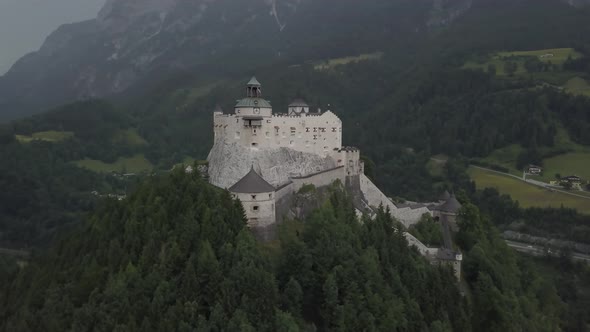 Aerial orbit of medieval Hohenwerfen Fortress on top of a steep hill, surrounded by pine forest and