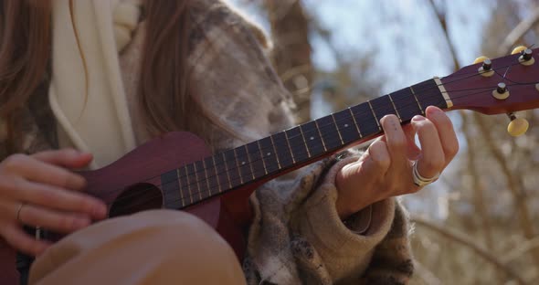 girl's hands play the ukulele at sunset in the forest. close-up