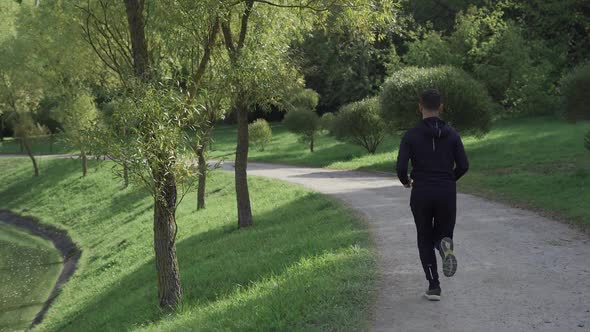 Back View Man Running Through Summer Forest Camera Following Runner in Wireless Headphones Healthy