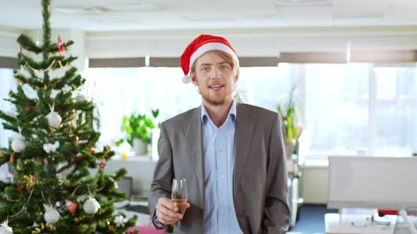 Handsome Young Blond Businessman Wearing Christmas Hat Holding Glass of Wine Smiling Coming Forward