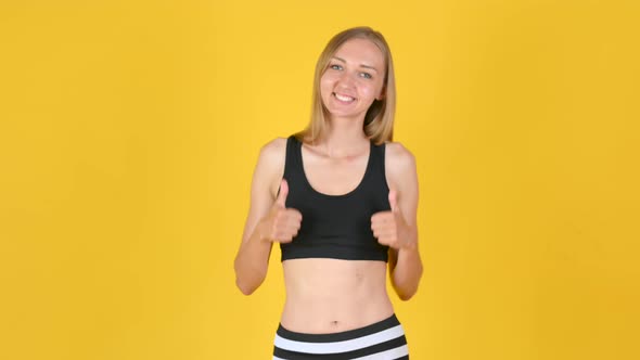 Happy Attractive Girl in Sportswear smiles and waves her hands showing thumb up