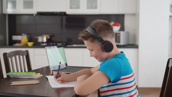 Boy in Headphones Doing Homework on Kitchen Table