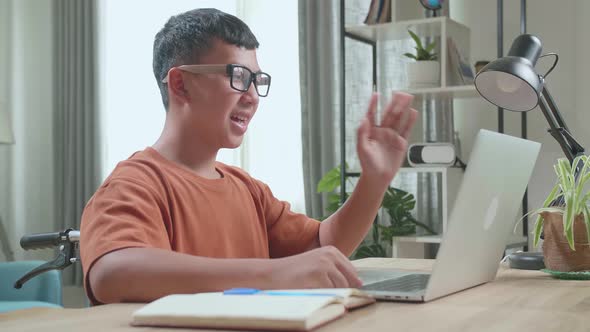 Young Asian Boy Sitting In A Wheelchair While Video Call On Laptop Computer At Home