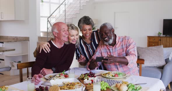 Diverse senior couples sitting by a table drinking wine eating dinner and taking a selfie