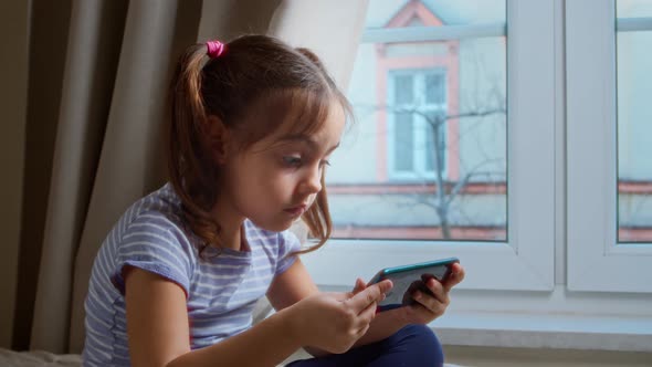 Cute Little Girl Uses Smartphone for Online Games and Watching Content