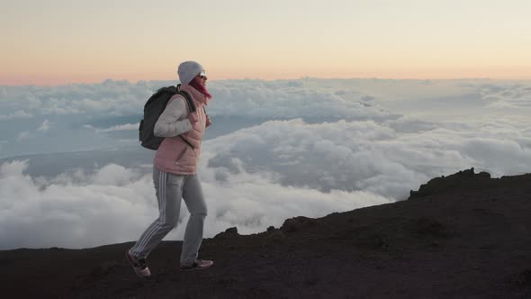 Happy Woman with Backpack Hiking Up Scenic Volcanic Mountain Peak at Pink Sunset