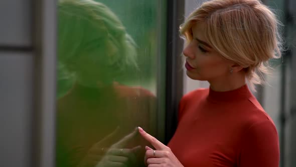 Portrait of a Blonde in Red Clothes and with Bright Lipstick on Her Lips. She Looks Into the Green