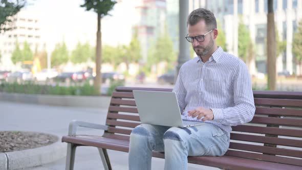 Young Adult Man Reacting to Loss on Laptop While Sitting Outdoor on Bench