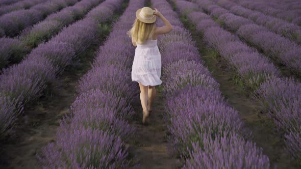 A Young Caucasian Woman Dressed in a Straw Hat and a Summer Sundress Runs in the Summer at Dawn