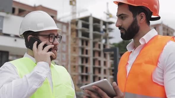 Happy Engineer Speaks on Mobile Phone on Construction Site and Checks the Work of the Worker