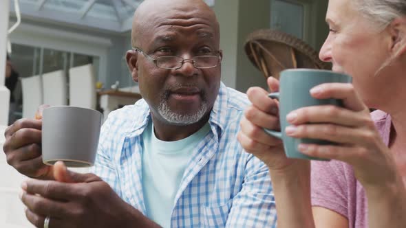 Happy senior diverse couple wearing shirts and drinking coffee in garden