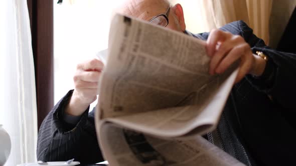 An Elderly Man Reads a Newspaper at a Table in a Cafe
