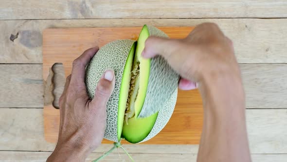 The man use knife split the green melon on wood plate