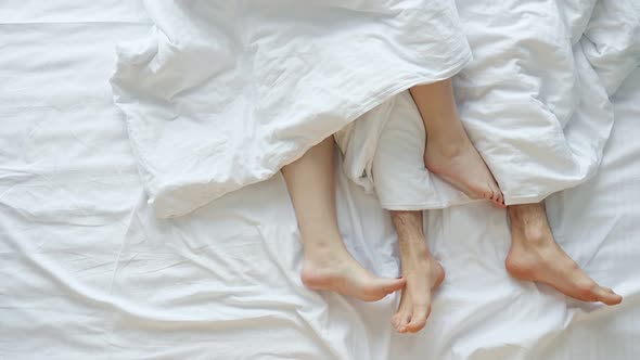 Couple Caresses Each Other Lying in Bed on White Sheets