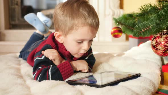 Little Boy Using and Playing on Digital Computer While Lying Next To christmas Tree