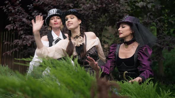 Three Caucasian Women in Steampunk Outfit Standing in Forest Touching Plants Talking in Slow Motion