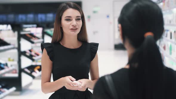 Front View of Young Woman Talking with Shop Assistant in Cosmetics Store