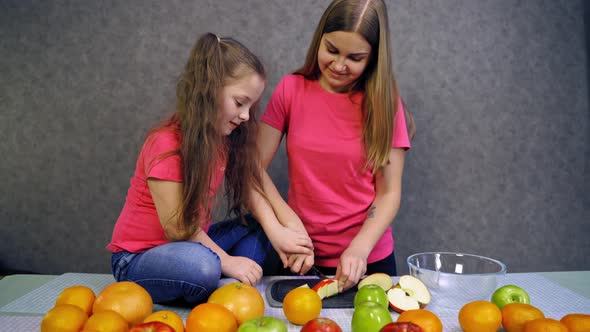 Girl making fruit salad. Girls sliced fruits for salad at the table