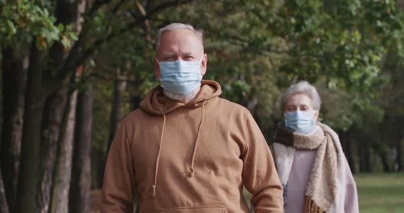 Adult Couple on Walk in a Forest Park, Autumn Day, Gray-haired Man and a Woman in Medical Masks