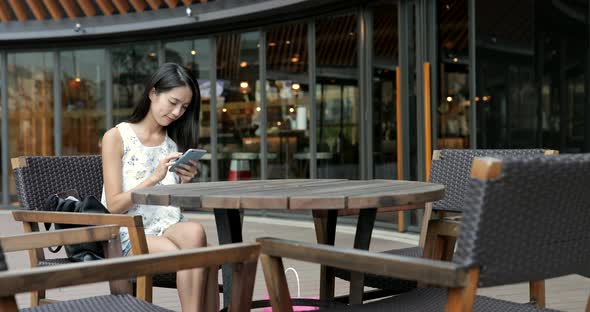 Woman using mobile phone and sitting at outdoor coffee shop