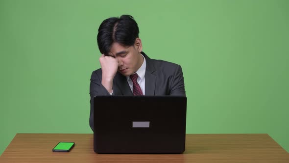 Young Handsome Asian Businessman Working with Laptop Against Green Background