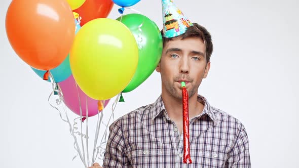 Young Caucasian Male with Dark Hair and Light Bristle on White Background Wearing Birthday Cap Sadly