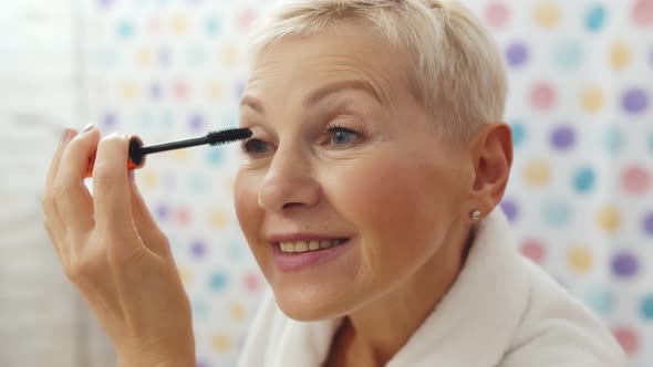 Mature Woman Putting Mascara Looking in Mirror Getting Ready in Morning