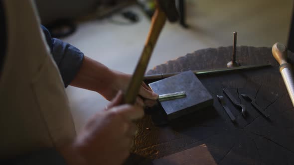 Close up of hands of caucasian female jeweller using hammer, making jewelry