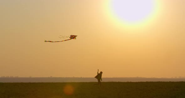 A Boy Is Playing with a Kite in the Sky at Sunset. 