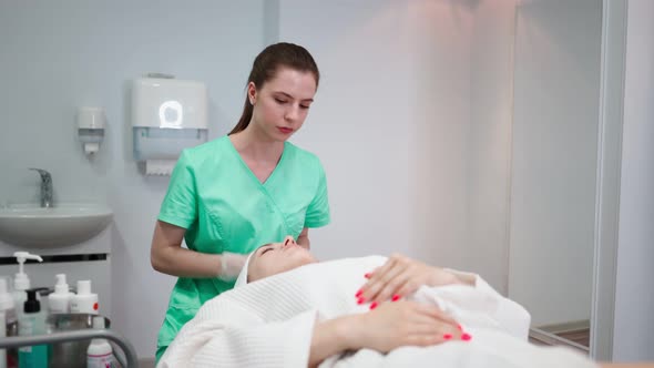 Girl Beautician Makes Facial Cleansing Procedure for Young Woman in Beauty Salon