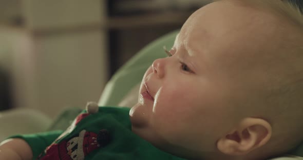 Close Profile View of Cute Toddler in Chair During Feeding with Spoon By Mother