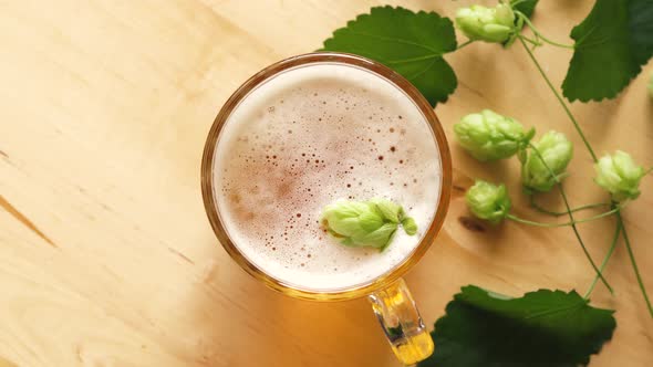 Top View of Mug of Beer with Foam and Hops on Bright Wooden Table