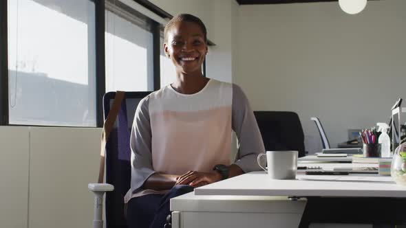Happy african american businesswoman sitting at desk and smiling at work