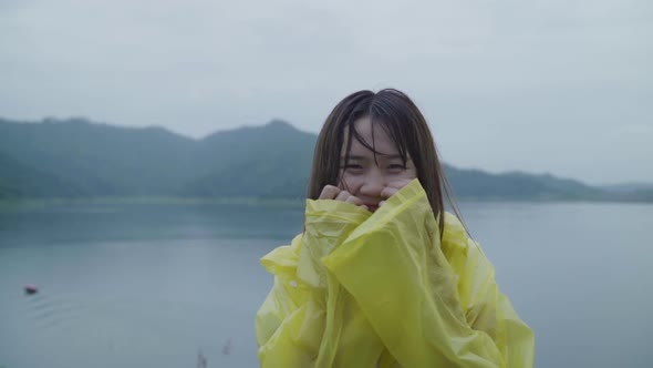 Young Asian woman feeling happy playing rain while wearing raincoat standing near lake.