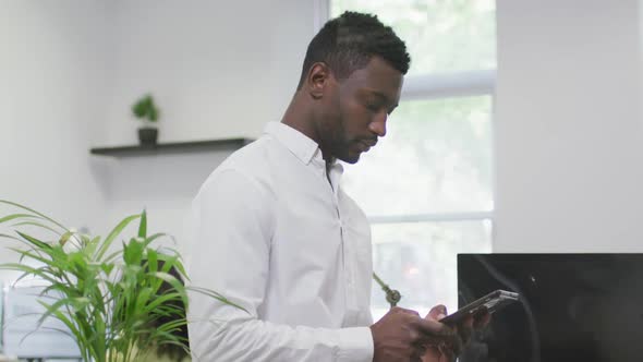 Thoughtful african american businessman using tablet, standing in empty modern office