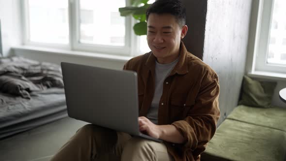 Smiling Asian man wearing casual cloth working on laptop