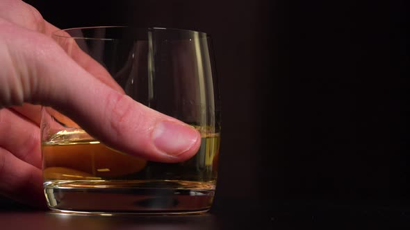 A Man Puts a Glass of Whiskey on a Table - Closeup - Dark Background