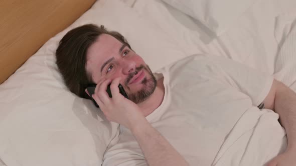 Casual Young Man Talking on Smartphone While Sleeping in Bed