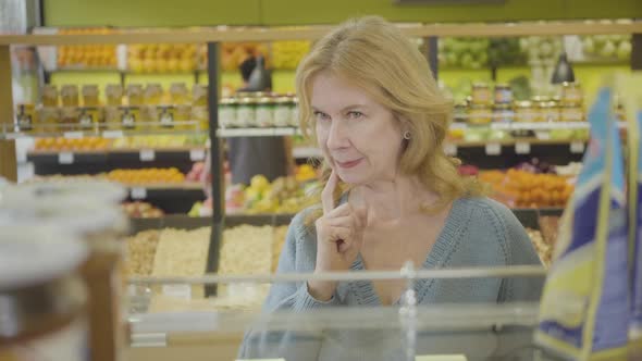 Portrait of Confident Adult Caucasian Woman Looking Through Shelves in Supermarket. Concentrated