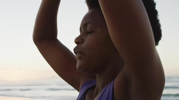 African american woman practicing yoga and meditating on sunny beach