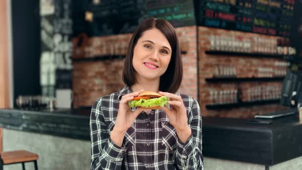 Portrait of Adorable Young Woman Posing Holding Fresh Appetizing Burger Looking at Camera