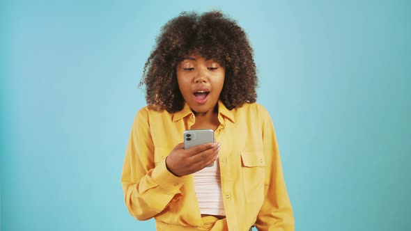 Afro American Woman Looking at Cellphone Saying Yes Raising Fists Up Being Surprised and Overjoyed