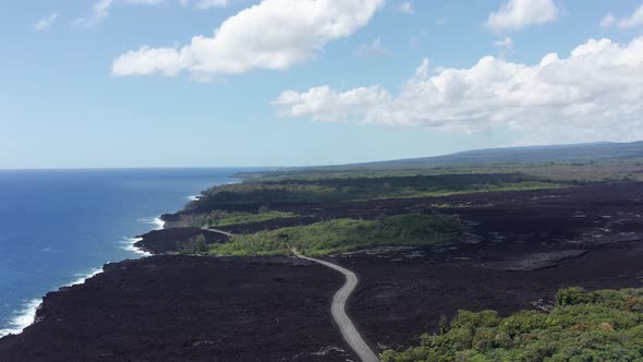 Wide aerial shot flying over a recently dried lava flow with a road cutting across it on the Big Isl